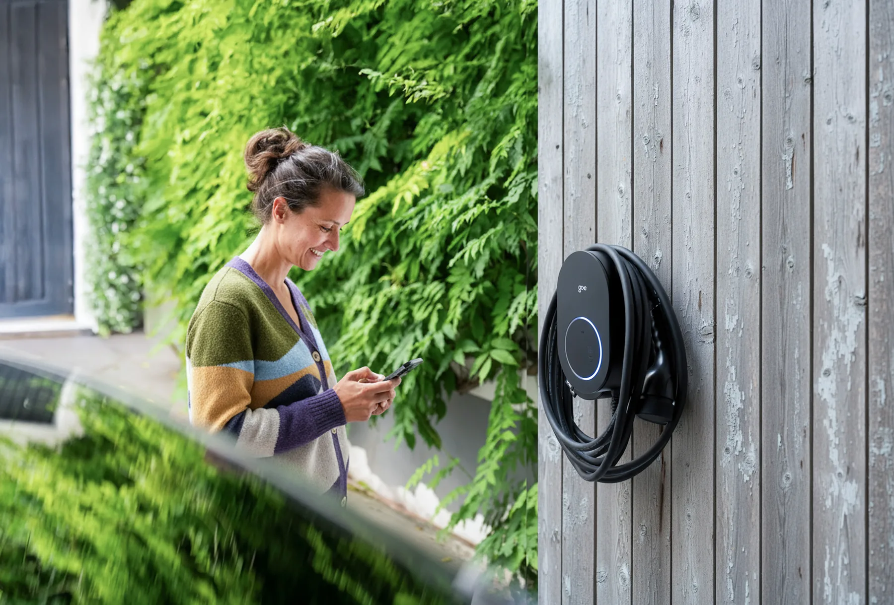 Kvinde styrer hjemmelader med app — go-e Charger Gemini flex 2.0 monteret på væg